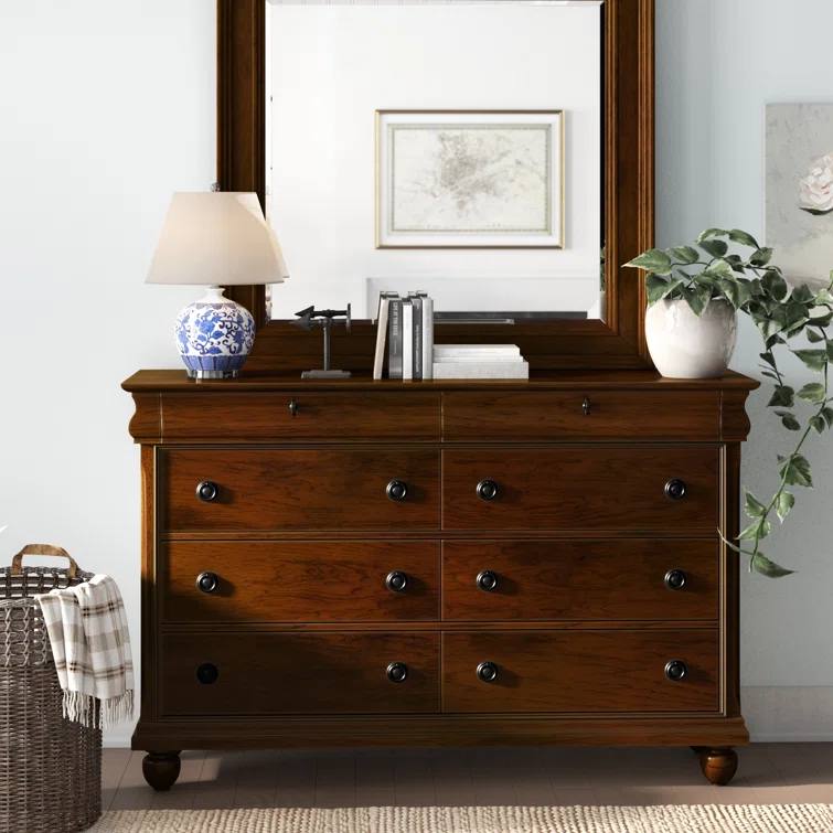 Rich cherry wood six-drawer traditional dresser with round brass knobs positioned in classic bedroom setting with mirror and decor