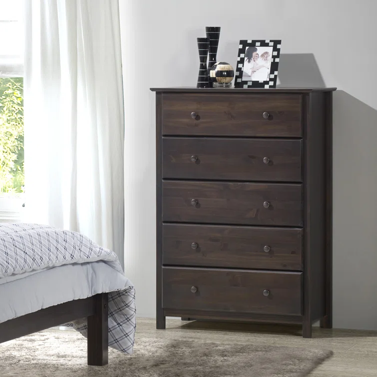 Dark walnut five-drawer chest of drawers with bronze hardware positioned next to bed in contemporary bedroom setting