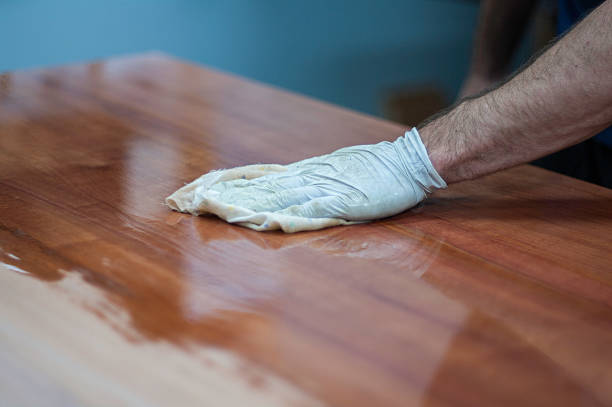 Gloved hand applying wood polish or cleaner to a polished wooden table surface, showing proper furniture care and maintenance.