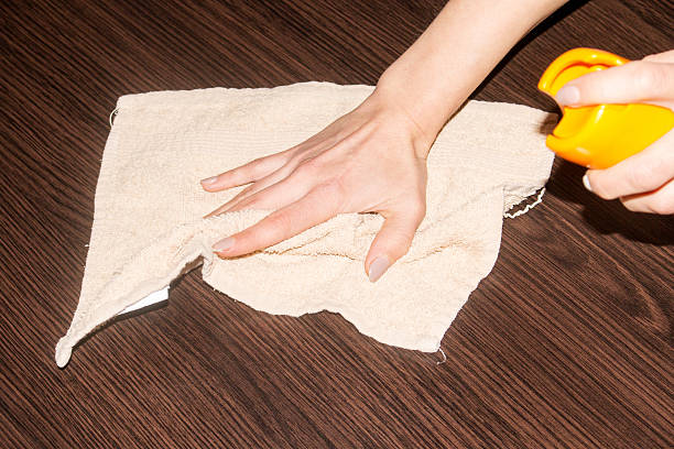 Hand using a soft cloth to polish a dark wooden table surface with lemon, demonstrating natural cleaning methods for wood furniture.