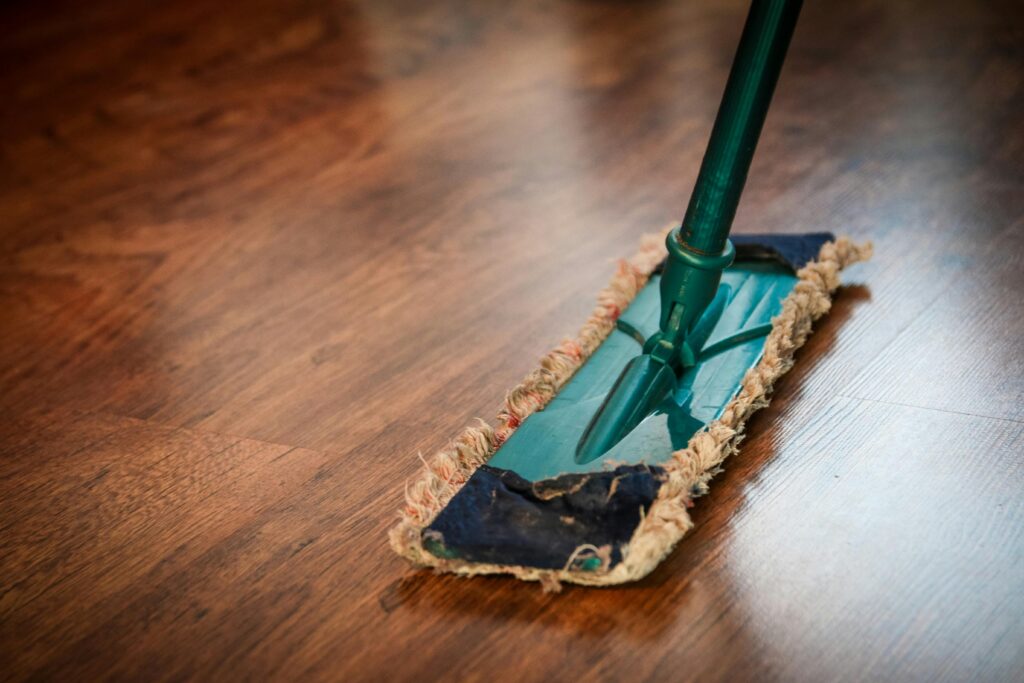 Close-up of a dust mop cleaning a hardwood floor, showing the proper tool for regular maintenance of wood surfaces.