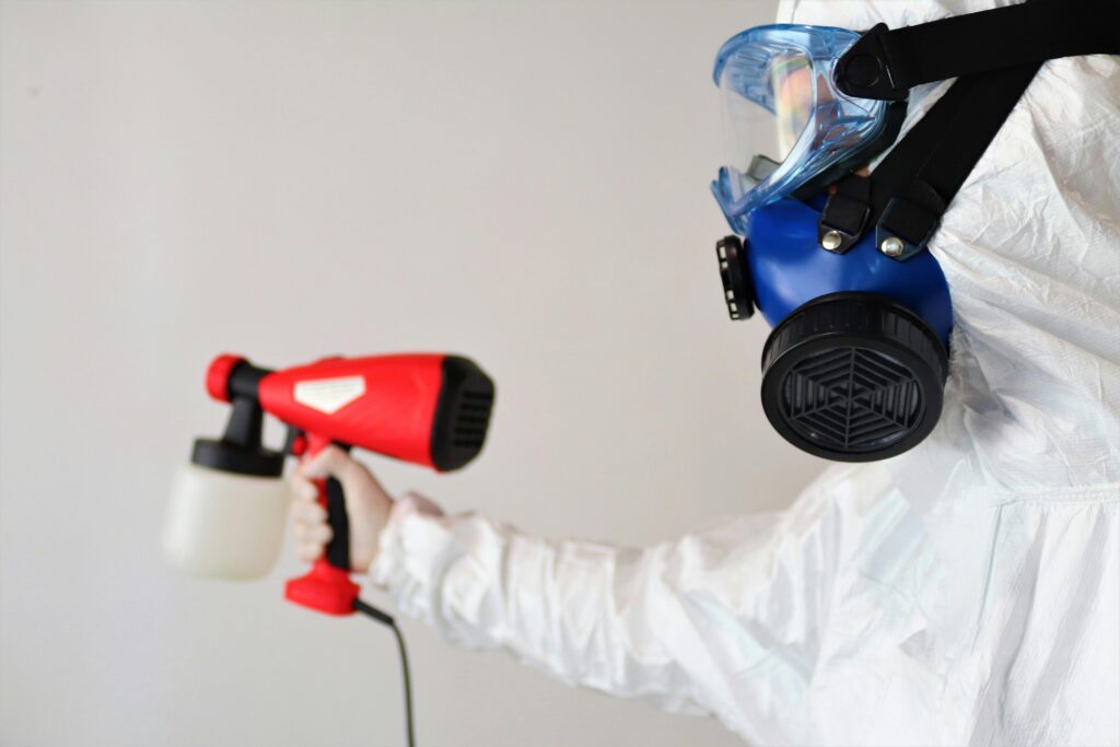 Person cleaning mold off a wall, using a respirator.