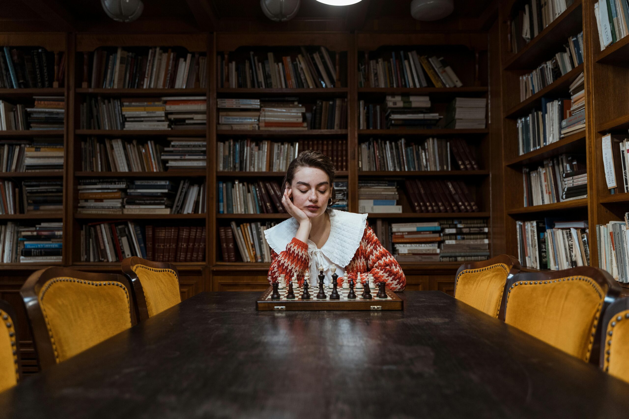 Wooden bookcase wall unit displaying extensive book collection in cozy reading room with chess table