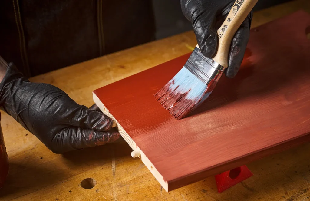Carpenter sanding wood for painting while wearing safety glasses, essential step before painting wooden furniture
